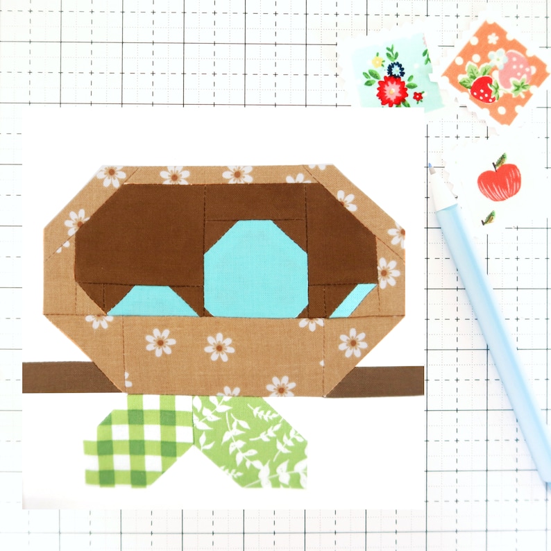 May include: A brown and tan fabric bird's nest with white flowers, a blue egg, and green leaves. The nest is on a brown branch.
