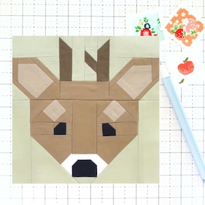 May include: A patchwork quilt block featuring a deer face with brown, beige, and black fabric pieces. The deer has large ears, a brown nose, and black eyes.