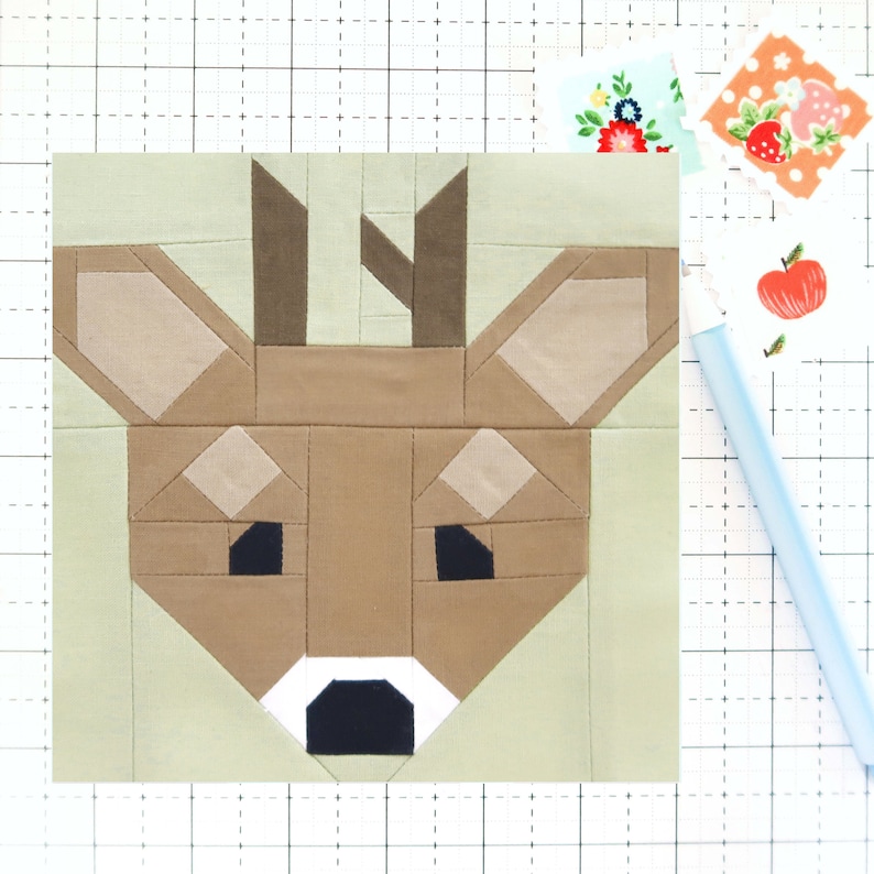 May include: A patchwork quilt block featuring a deer face with brown, beige, and black fabric pieces. The deer has large ears, a brown nose, and black eyes.