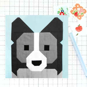 May include: A fabric square featuring a geometric dog face design in shades of gray, black, and white, set against a light blue background. The dog's face is constructed from various fabric shapes, creating a pixelated effect. Decorative floral and fruit stickers are in the background.