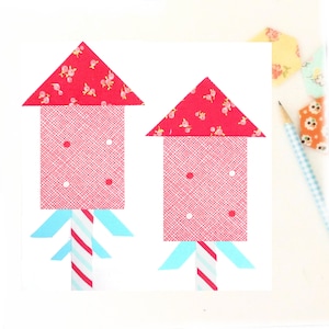 May include: Two red and white fabric rockets with blue and white striped bases. The rockets are made of different patterned fabrics, one with small white flowers and the other with a white polka dot pattern.