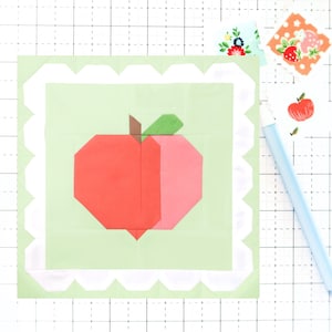 May include: A green fabric square with a white scalloped border. A red and pink apple is centered on the square.