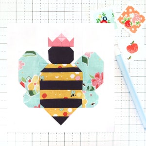 May include: A patchwork bee with a pink crown, yellow and black stripes, and a light blue and floral patterned body. The bee is on a white background.