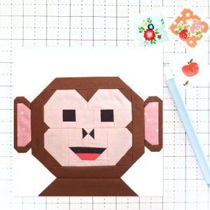 May include: A brown and pink fabric monkey face with a red mouth and black eyes. The monkey is made of fabric squares sewn together.
