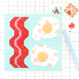 Op de afbeelding: Een quiltblok met een rood en roze zigzagpatroon aan de linkerkant en twee witte en roze bloemmotieven aan de rechterkant. Het quiltblok bevindt zich op een lichtblauwe achtergrond.