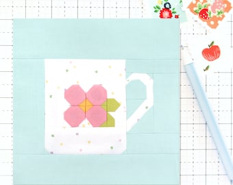 May include: A light blue fabric square with a white mug with a pink flower on it. The mug is surrounded by a white border.
