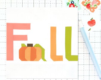 Puede incluir: Una tarjeta blanca con la palabra "FALL" escrita en letras de papel de colores. La letra "A" está reemplazada por una pequeña calabaza naranja.