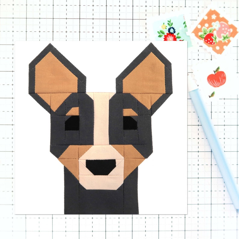 May include: A black, brown, and beige patchwork fabric dog head with a geometric design. The dog has large ears and a small nose.