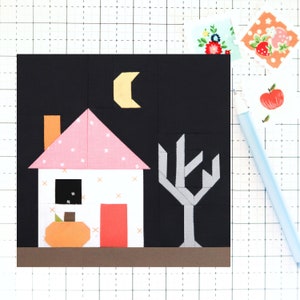 May include: A white house with a pink roof and a brown chimney, a gray tree, a yellow crescent moon, and an orange pumpkin in front of the house against a black background.