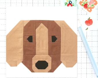 Könnte beinhalten: Ein brauner und schwarzer Patchwork-Stoffhundekopf mit einem einfachen geometrischen Design. Die Augen, die Nase und die Ohren des Hundes sind alle schwarz umrandet.