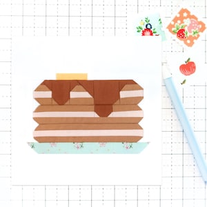 Könnte beinhalten: Ein Stapel brauner und rosa gestreifter Pfannkuchen mit einem Klecks braunem Sirup und einem gelben Quadrat Butter darauf. Die Pfannkuchen liegen auf einem hellblauen und weißen Teller mit Muster.