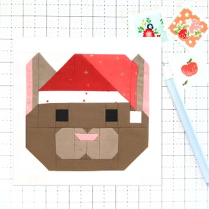 Puede incluir: Una aplicación de tela de patchwork marrón y rosa de un oso con un gorro de Papá Noel rojo y blanco.