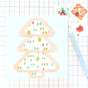 May include: A light blue card with a three-tiered paper Christmas tree. The tree is made of white fabric with a green and blue pattern and has a peach-coloured border.