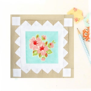 May include: A beige fabric square with a white border and a smaller square in the centre. The centre square is light blue with a pink and red floral print.