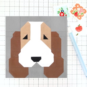 May include: A brown and white patchwork dog face with black eyes and nose. The dog face is on a gray background.