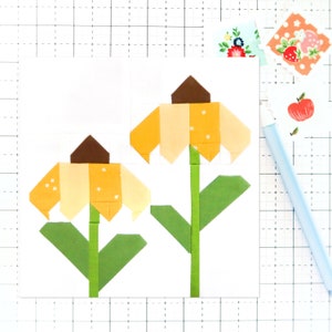 Peut inclure: Deux fleurs en papier jaune et brun avec des tiges et des feuilles vertes sur un fond blanc.