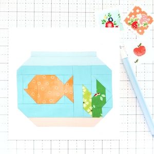 May include: A blue and orange fabric fishbowl with a green and white fabric plant inside. The fishbowl is made of fabric squares sewn together.