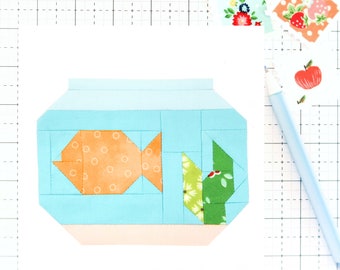 May include: A blue and orange fabric fishbowl with a green and white fabric plant inside. The fishbowl is made of fabric squares sewn together.