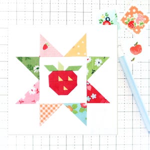 Może przedstawiać: Białe tło z czerwono-żółto-zielonym blokiem patchworkowym z czerwoną truskawką w środku. Blok patchworkowy składa się z ośmiu trójkątów i kwadratu.