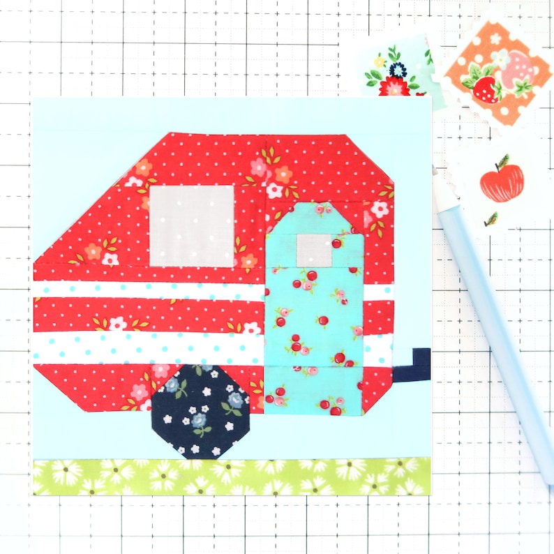 May include: A red and white striped camper with a blue and white floral pattern on the side. The camper has a white window and a green grass patch underneath.
