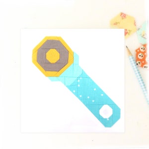 May include: A blue and yellow fabric patchwork design of a spanner tool. The spanner is made of fabric squares sewn together in a geometric pattern.