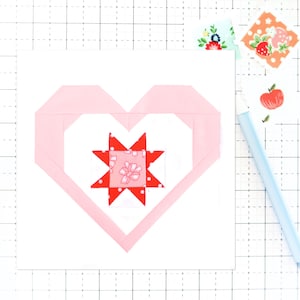 May include: A pink heart-shaped fabric applique with a red and white star in the center. The star is made of smaller fabric squares with a pink and white floral pattern.