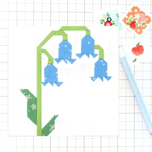 May include: A blue and green fabric applique of a flower with five bell-shaped blooms. The flower is on a white background.