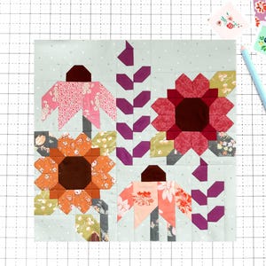 May include: A square quilt block featuring a light mint green background with white polka dots. The design displays four floral motifs in shades of orange, pink, red, and dark purple, accented by green leaves and stems, alongside a light blue pencil.