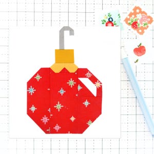 May include: A red and yellow paper ornament with a white snowflake pattern. The ornament has a silver hook.