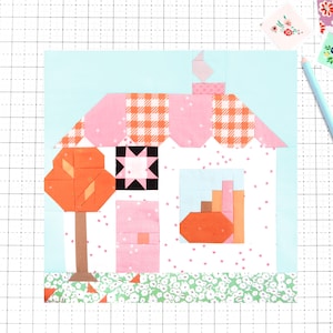 May include: A quilt block pattern featuring a house with a pink gingham roof, a white wall with pink speckles, a brown tree, and a pumpkin in the window. The design includes a black star motif, a light blue sky, and a green floral ground.