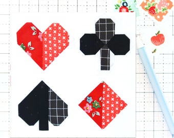 May include: A white card featuring four playing card suits: heart, club, spade, and diamond. The heart and diamond are red with floral patterns, while the club and spade are black with white grid patterns. A light blue pen and decorative stickers are also visible.