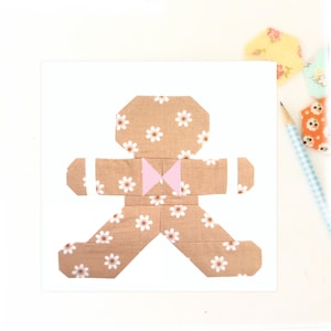 May include: A brown gingerbread person with a pink bow tie, made from fabric with a white daisy pattern.