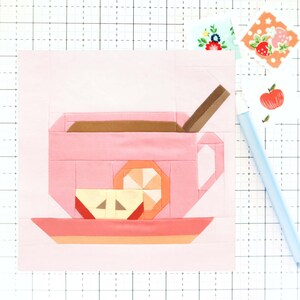 May include: A pink teacup with a brown handle and a brown rim filled with brown liquid. A brown stick is in the teacup. A slice of orange and a slice of apple are on a pink saucer.