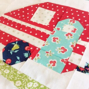 May include: A patchwork quilt block featuring a red, white, and blue camper design. The camper has a white roof with red polka dots, a red body with white stripes, and a blue and white floral side panel. The quilt block is made with a variety of fabrics and is perfect for a child's room or a camping-themed project.