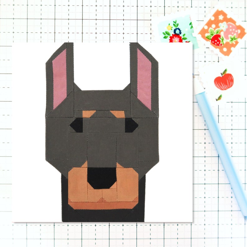 May include: A patchwork quilt block featuring a dog's face. The dog has brown ears, a black nose, and a brown muzzle. The background is white.
