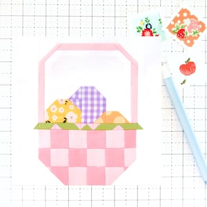 May include: A pink fabric basket with a checkered pattern, filled with three fabric Easter eggs. The eggs are yellow with white flowers, purple with white gingham, and orange with white stripes.