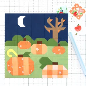 May include: A patchwork quilt block featuring a fall scene with orange pumpkins, a brown tree, and a crescent moon against a dark blue sky. The pumpkins have floral and striped patterns. Green grass fills the foreground.