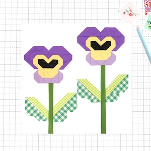 May include: Two paper-crafted pansy flowers with purple petals, yellow and black centers, and green stems with gingham accents. The flowers are on a white background with a grid pattern, accompanied by small floral stickers and a blue pencil.