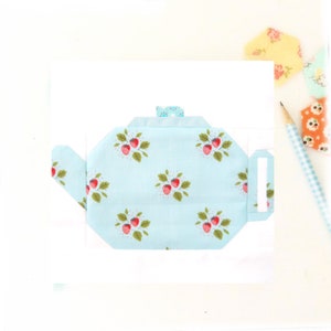 May include: A light blue teapot with a white and red strawberry pattern. The teapot has a small handle and a lid.
