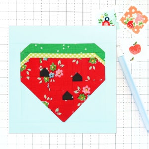 May include: A red and green fabric watermelon applique on a light blue background. The watermelon is made of small squares of fabric and has black seeds.