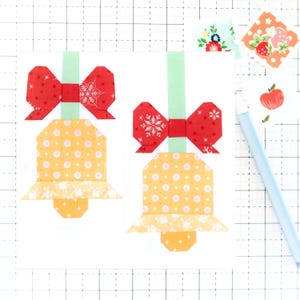 Puede incluir: Dos campanas amarillas y naranjas con lazos rojos y tallos verdes. Las campanas tienen lunares blancos y los lazos tienen patrones de copos de nieve blancos.