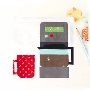 May include: A red coffee mug with white polka dots sits next to a gray and black coffee maker with a brown pot and a blue lid. The coffee maker has a green and white patterned top.