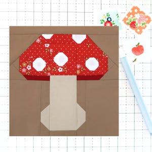 May include: A brown fabric square with a red and white mushroom applique. The mushroom has a red cap with white polka dots and white circles. The stem is beige.