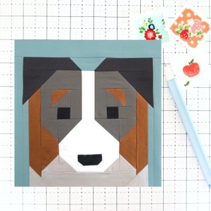 May include: A patchwork quilt block depicting a dog's face. The block is made of various fabrics in shades of brown, gray, white, and black. The dog's face is surrounded by a light blue border.