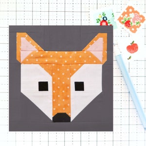 May include: A patchwork fox head made of fabric squares in orange with white polka dots, pink, white, and black. The fox head is on a gray background.