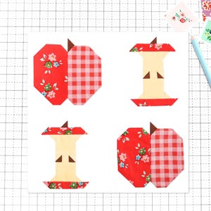 Peut inclure: Quatre blocs de courtepointe en tissu disposés en carré sur une grille. Deux blocs représentent des pommes entières en tissu floral rouge et vichy rouge, tandis que deux blocs montrent des trognons de pomme en crème, floral et vichy rouge.