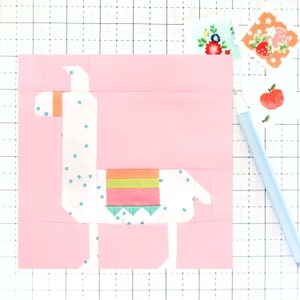 May include: A pink fabric square with a white llama applique. The llama has a light orange, green, and pink striped saddle and a white body with blue polka dots.