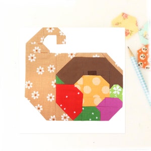 May include: A patchwork quilt block in the shape of a spiral, featuring various colours and patterns, including brown, yellow, red, green, and purple.