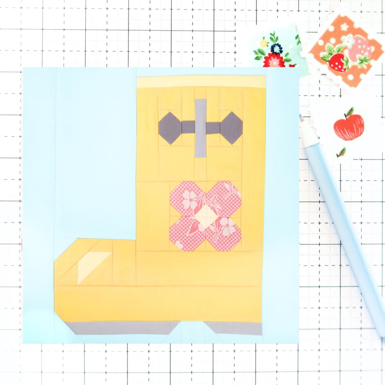 May include: A yellow paper boot with a pink and white floral design and a gray buckle. The boot is on a light blue background.