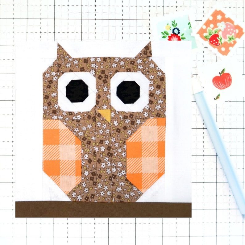 May include: A brown owl with orange and white checkered wings, brown floral body, and black eyes. The owl is sitting on a brown branch.